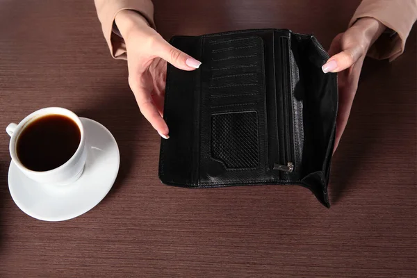 An empty purse in a woman's hands.White porcelain coffee Cup on the table. The concept of the financial crisis. Unrecognizable photo without a face. Top view. Copy space.