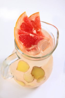 Beyaz arka planda uzun cam bir sürahi içinde greyfurt dilimleri ve zencefil dilimli limonata. Dikey fotoğraf. İzole bir nesne. Üst görünüm.