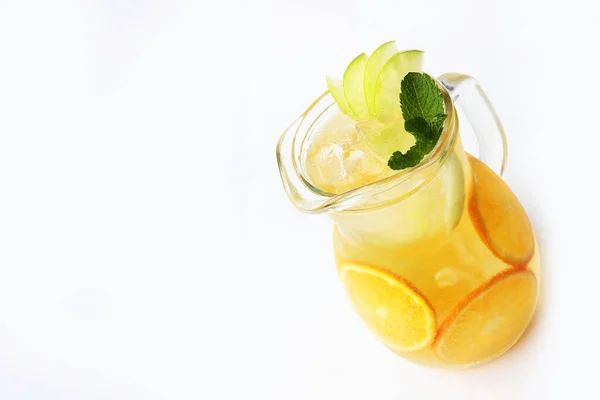 Lemonade of oranges and apples with mint in a tall glass jug on a white background. An isolated object. — Stock Photo, Image