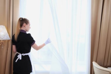 Bir kadın daireyi havalandırıyor. Pencerenin yanında tanınmayan bir fotoğraf var. Otelde ya da evde temizlik ve hijyen kavramı. Boşluğun kopyası.