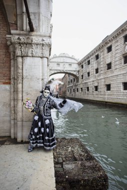 Karnaval maskeli bir kişi arka planda iç çekiş köprüsü olan bir binanın duvarına yaslanıyor Venedik İtalya