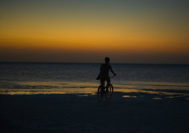 Gün batımında Meksika 'da Holbox adasında bisiklet sürmek. İnsanlar gün batımında Karayip plajında bisiklet sürüyor..