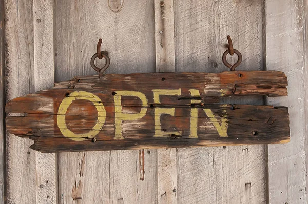 Wooden signboard open with rope hanging on planks background. Old wooden hanging on the wooden door open with a text