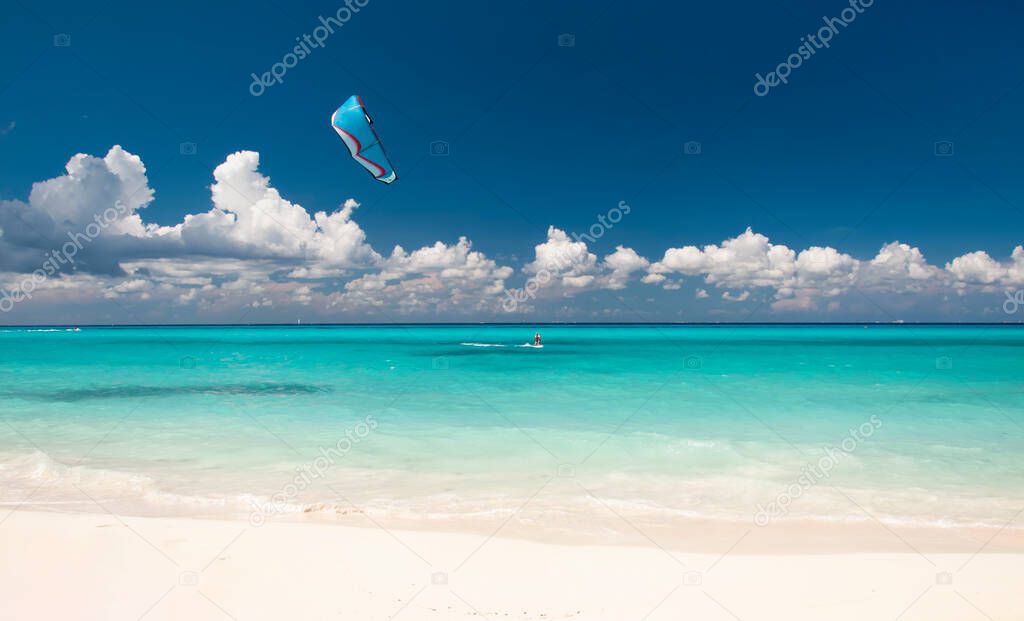 Kitesurfer with Kiteboard in front of an amazing and deserted tropical beach, on the horizon the blue sky and white clouds