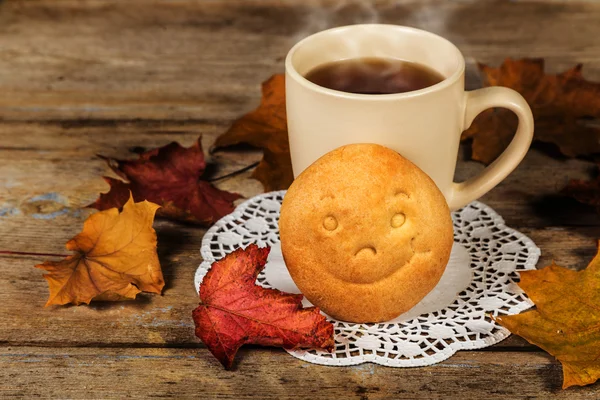 Hot drink, biscuit with a smile and autumn leaves — Stockfoto