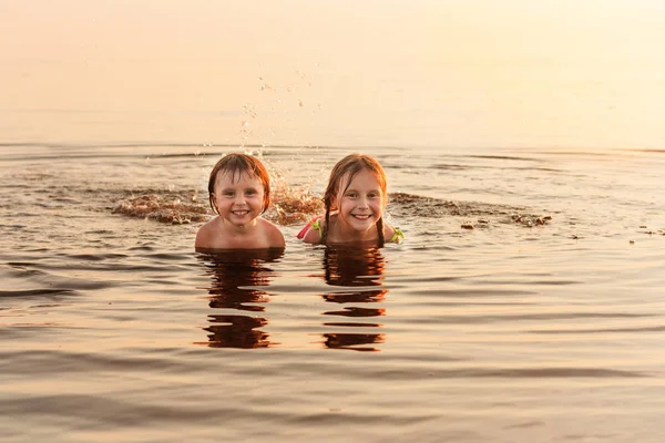 Two lovely little sisters bathe in the sea in the evening, lit by the setting sun — Stock Photo, Image
