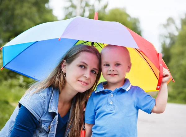 Retrato de una madre con su hijo bajo un paraguas de arco iris sobre un fondo natural — Foto de Stock