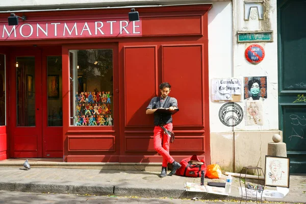 Montmartre 'da bir sanat galerisinin cephesine yaslanmış bir adam çiziyor. Turistlere karikatür öneriyor. Paris, Fransa.                             