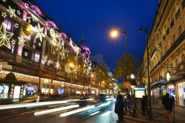Geceleri Haussmann Bulvarı 'ndaki Printemps mağazasında. Ön cephede Noel süsleme ışıkları ve kalabalık bulvarda trafik ışıkları. Paris, Fransa.