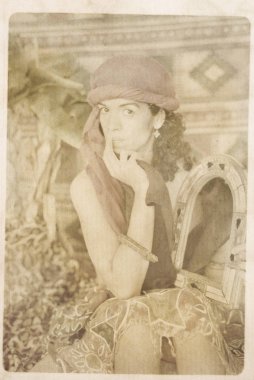 Şiş başörtülü genç bir doğulu kadın oturuyor ve elinde mücevherli bir ayna tutuyor. Arka planda halı ve palmiye yaprakları var. Kağıt dokusuyla solmuş retro sepia görünümü.