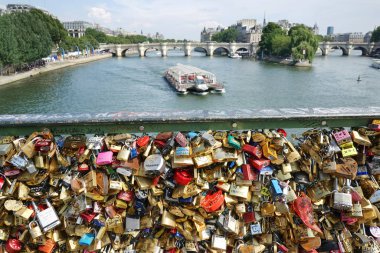 Aşk kilitleri Pont des Arts köprüsünün korkuluklarına bağlı. Arka planda soldan sağa, mavi bayraklı Paris-Plages plajı, Pont Neuf köprüsü ve Ile de la Cite. İki köprü arasında gezici bir tekne. Paris, Fransa.