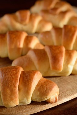 Tahta kesme tahtalarına yerleştirilmiş birkaç kruvasanın ilkine yakın plan. Koyu kahverengi ahşap masa. Otlatıcı ışık.