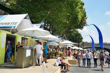 Snacks and refreshments stalls during the Paris-Plages season. People strolling by the Seine river. Parts of the pont au Change, the green pont Notre-Dame bridges. The green Bouquinistes stalls on the upper left till the bridge. Paris, France. 