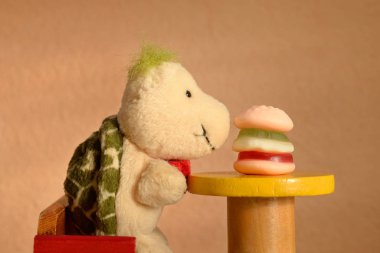 Bir hamburgerle yüz yüze masada oturan yumuşak bir oyuncak kaplumbağa. Çocuklar fast food yiyor, abur cubur konsepti.