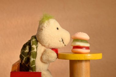 A soft toy turtle sitting at a table face to face with a hamburger. Children eating fast food, junk food concept. clipart