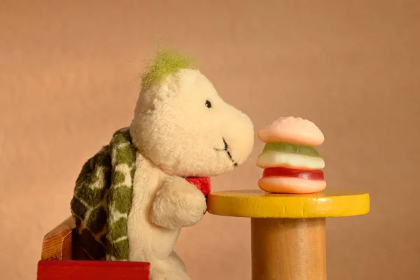 Bir hamburgerle yüz yüze masada oturan yumuşak bir oyuncak kaplumbağa. Çocuklar fast food yiyor, abur cubur konsepti.