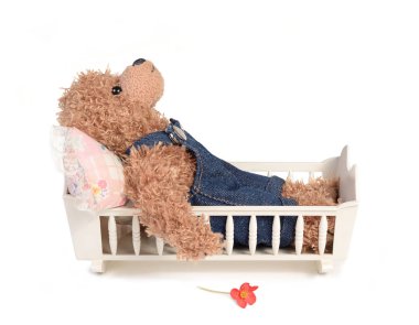 A Teddy bear wearing a jeans overall is lying in bed. A red flower on the ground. Isolated on white background. Depression, lovesick or overworked concept. clipart
