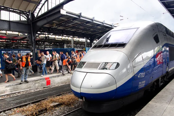 Paris-Est tren istasyonu. Demiryolu işçileri bir TGV tren motorunun yanında çalışıyorlar. Platformda bavulla yürüyen gezginler. Gare de l 'Est, Paris, Fransa.