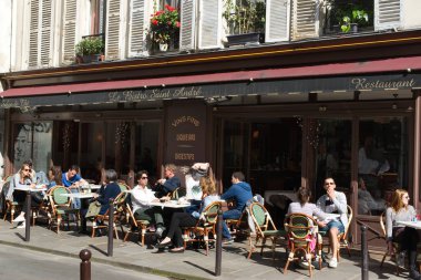 İnsanlar bir bistro kafenin terasında oturup Nisan güneşinin tadını çıkarıyorlar. Saint-Germain-des-Pres, Quartier Latince, Paris, Fransa.