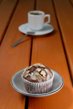 Tahta masadaki malzemelerin içinde dilimlenmiş badem ve kayısı reçeli ile ev yapımı çikolatalı kek. Arka planda kahve dolu beyaz bir espresso fincanı ve fincan tabağı. Boşluğu kopyala.