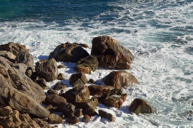 Uçurumun dibinde dalgalı deniz büyük karanlık kayalara çarpıyor.