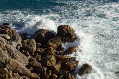 Uçurumun dibinde dalgalı deniz büyük karanlık kayalara çarpıyor.