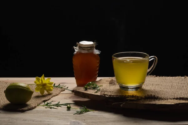 Lemon tea with honey in a glass cup. Hot healthy beverage on black background. Immune defense, vitamin c.