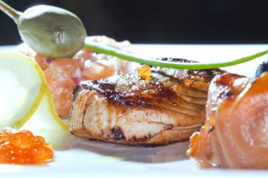 Kızarmış balık, havyar, limon, koyu arkaplanda kiraz domatesleri ve kapari stüdyolarıyla süslenmiş makro lezzetli bir yemek.