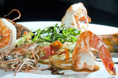 Siyah arka plan stüdyosundaki beyaz tabakta otlarla kaplı makro karidesler.