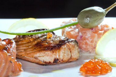 Kızarmış balık, havyar, limon, koyu arkaplanda kiraz domatesleri ve kapari stüdyolarıyla süslenmiş makro lezzetli bir yemek.