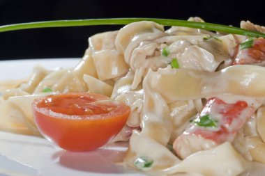 Soslu makro makarna ve domatesler arka plandaki karanlık bir stüdyoda beyaz tabakta.