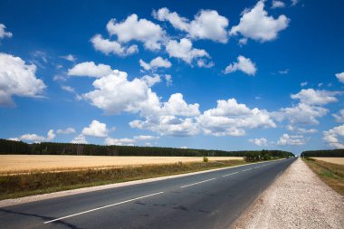 Yaz yolu tarlaların arasında ve açık mavi gökyüzü güneşli bir günde beyaz bulutlarla