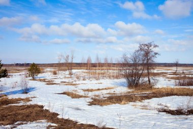 Geniş tarlalarda kar eriyor ilkbaharın başlarında, bulutlu bir günde gün batımında.
