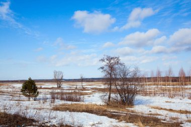 Geniş tarlalarda kar eriyor ilkbaharın başlarında, bulutlu bir günde gün batımında.