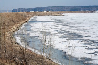 Nehir manzarası diseksiyonu ve ilkbaharın başlarında buz sürüklenmesi, kıyıdaki yapraksız ağaçlar ve bulutlu gökyüzü