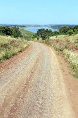 Yaz manzaralı toprak yol, mavi gökyüzü ve ufuktaki nehir güneşli bir günde