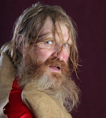 Kırmızı gömlek stüdyosunda uzun sakallı, bıyıklı ve ıslak sarı saçlı kutsanmış birinin yakın plan portresi.