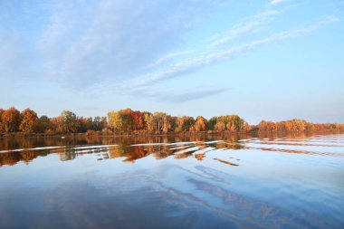 Sonbahar manzarası nehirde güzel bir sabah kumsalda renkli ağaçlar ve mavi gökyüzünde bulutlar.