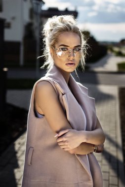 Ping ceketli ve gözlüklü genç bir kadın seksi bir elbiseyle sokakta yürüyor.