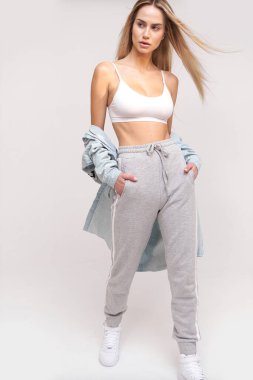 Spor tarzında güzel bir kadın. Bronz tenli, beyaz bluzlu ve gri pantolonlu.