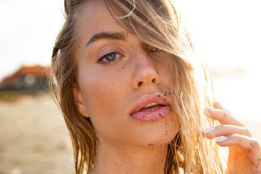 Güzel seksi manken siyah bir mayoyla siyah kumsalda uzanıyor. Uzun sarı saçlı, muhteşem göğüsleri ve dolgun dudakları var. Bali adasında sağlıklı okyanus dalgaları bulutları.