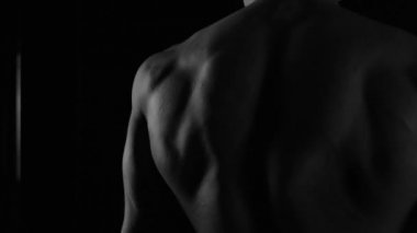 Güçlü vücut geliştirici kontrastlı ışık altında poz veriyor ve antrenman yapıyor. Vücudu ve üzerindeki tüm kasları su altında ve yavaş yağmurda gösteriyor.