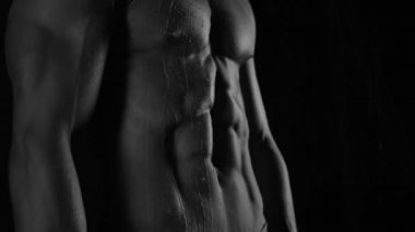 Güçlü vücut geliştirici kontrastlı ışık altında poz veriyor ve antrenman yapıyor. Vücudu ve üzerindeki tüm kasları su altında ve yavaş yağmurda gösteriyor.