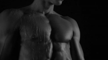 Güçlü vücut geliştirici kontrastlı ışık altında poz veriyor ve antrenman yapıyor. Vücudu ve üzerindeki tüm kasları su altında ve yavaş yağmurda gösteriyor.