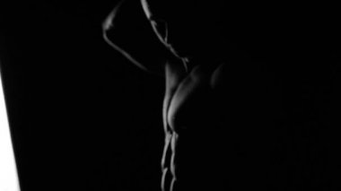 Güçlü vücut geliştirici kontrastlı ışık altında poz veriyor ve antrenman yapıyor. Vücudu ve üzerindeki tüm kasları su altında ve yavaş yağmurda gösteriyor.