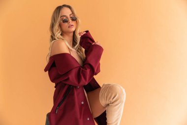 Mükemmel zayıf vücutlu seksi sarışın manken. Kocaman göğüsleri var. Bej kombikli ve parlak kırmızı ceketli.