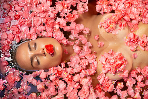 Красивая тощая сексуальная девушка с длинными волосами, полными губами и большой грудью лежит в ванне с расслабляющей здоровой флорой в спа-центре отеля, заботясь о своем теле и здоровье
