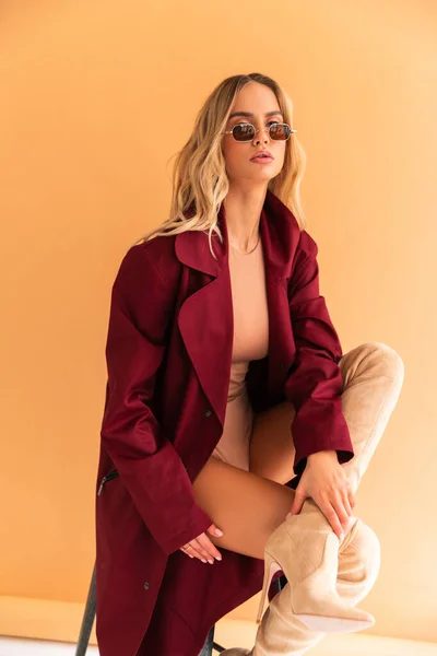 Sexy Blonde model with perfect skinny body with huge boobs posing in beige combidress and glam red coat so good fashion style retouched in very high quality