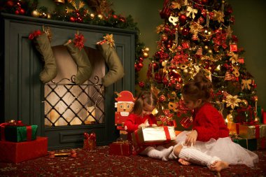 Küçük bir kız uçan bir hediye yakalıyor gülümsüyor ve Noel 'i ve bayramı bekliyor rahat bir ev, yanan bir şömine ve bir Noel ağacı.