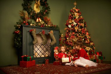 Küçük bir kız uçan bir hediye yakalıyor gülümsüyor ve Noel 'i ve bayramı bekliyor rahat bir ev, yanan bir şömine ve bir Noel ağacı.